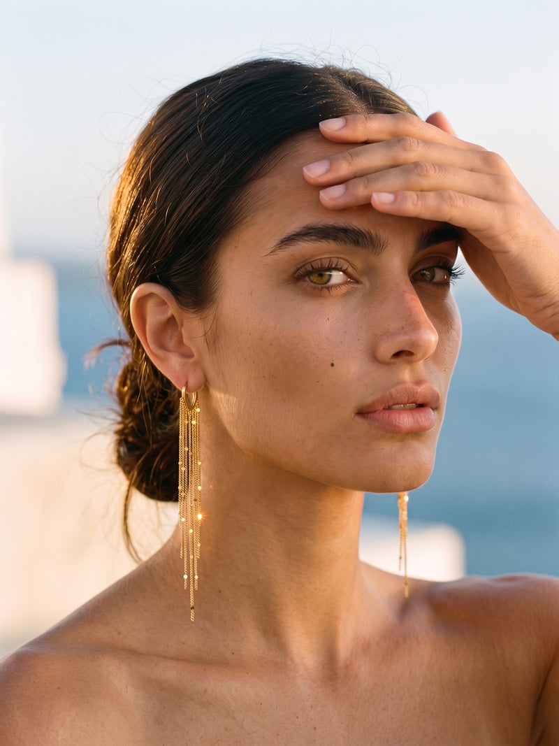 Boucles d'oreilles Cascade SORELI portées — créole en V plaquée or 18 carats avec franges de chaînes, portrait golden hour